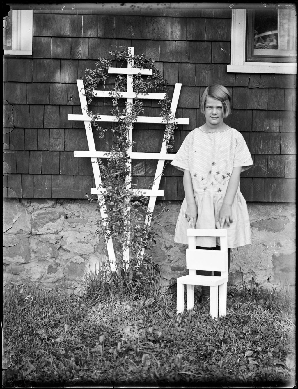 Miniature of Young Girl Standing With A Child's Chair And Next To A Trellis Outside A House
