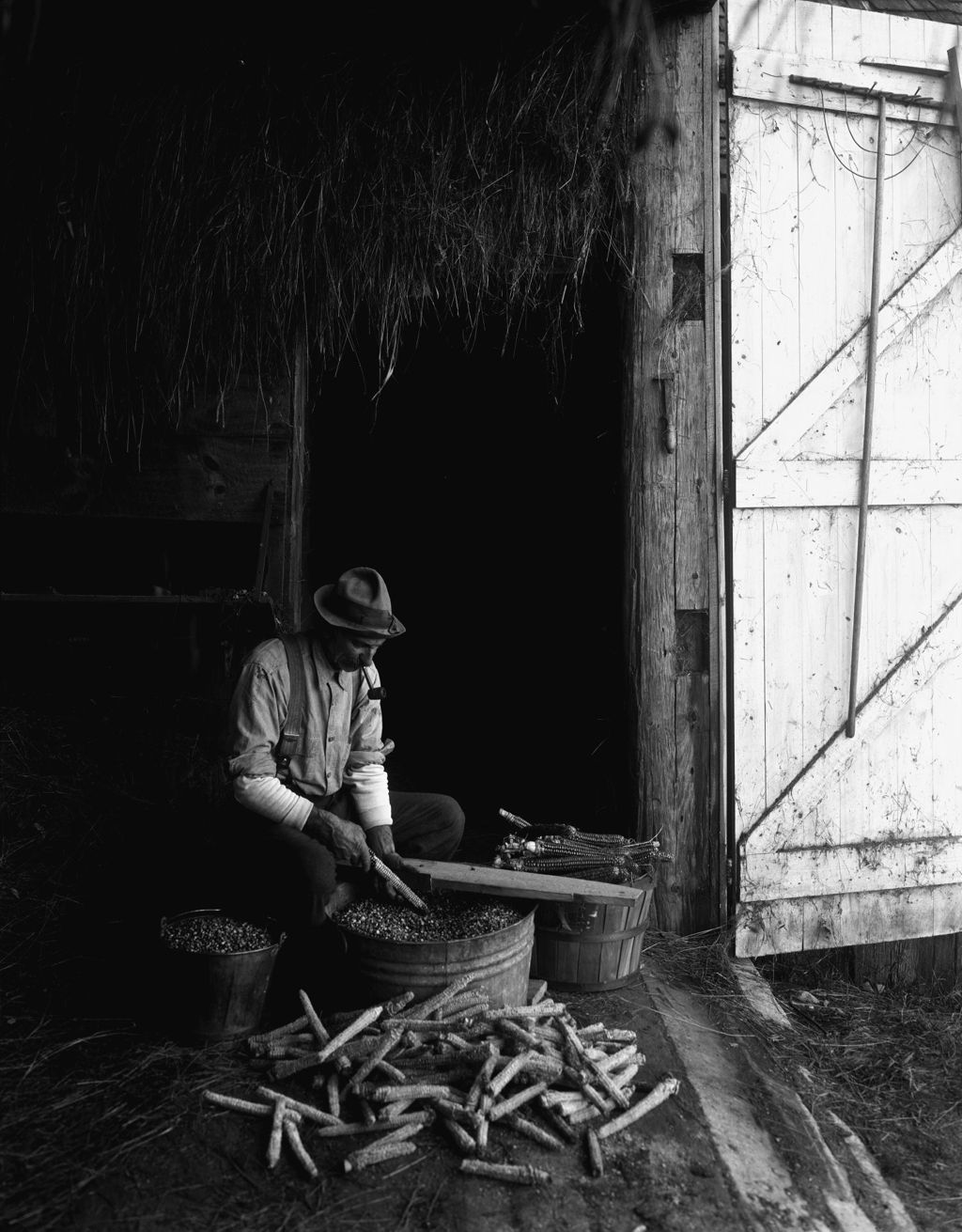 Miniature of Farmer Sitting In Doorway Of A Barn, He Is Hulling Corn Into A Tub In Porter