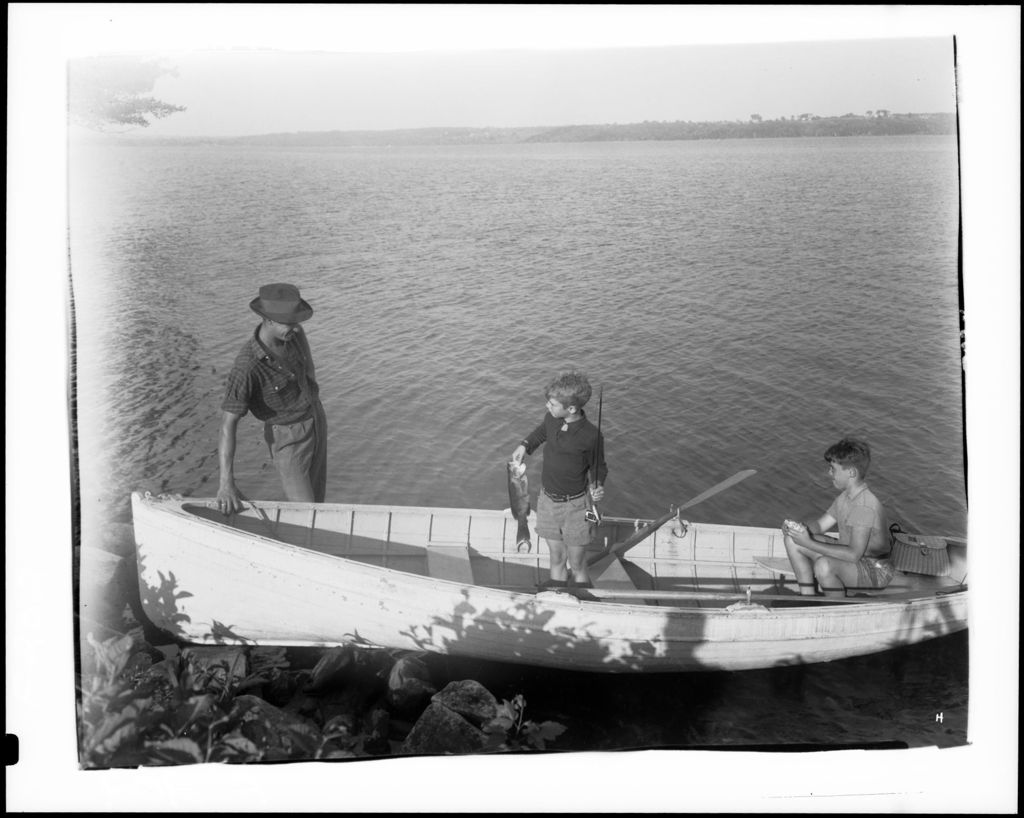 Miniature of Two Boys In A Boat Near Shore, One Holding A Fish He Caught While Talking To A Man On Shore