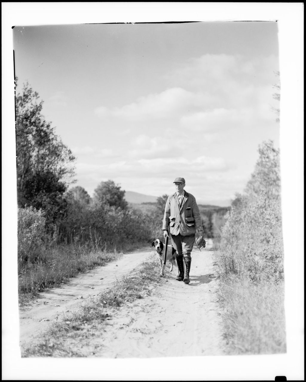 Miniature of Hunter And Dog Walking Down A Dirt Road, Mountains In Background