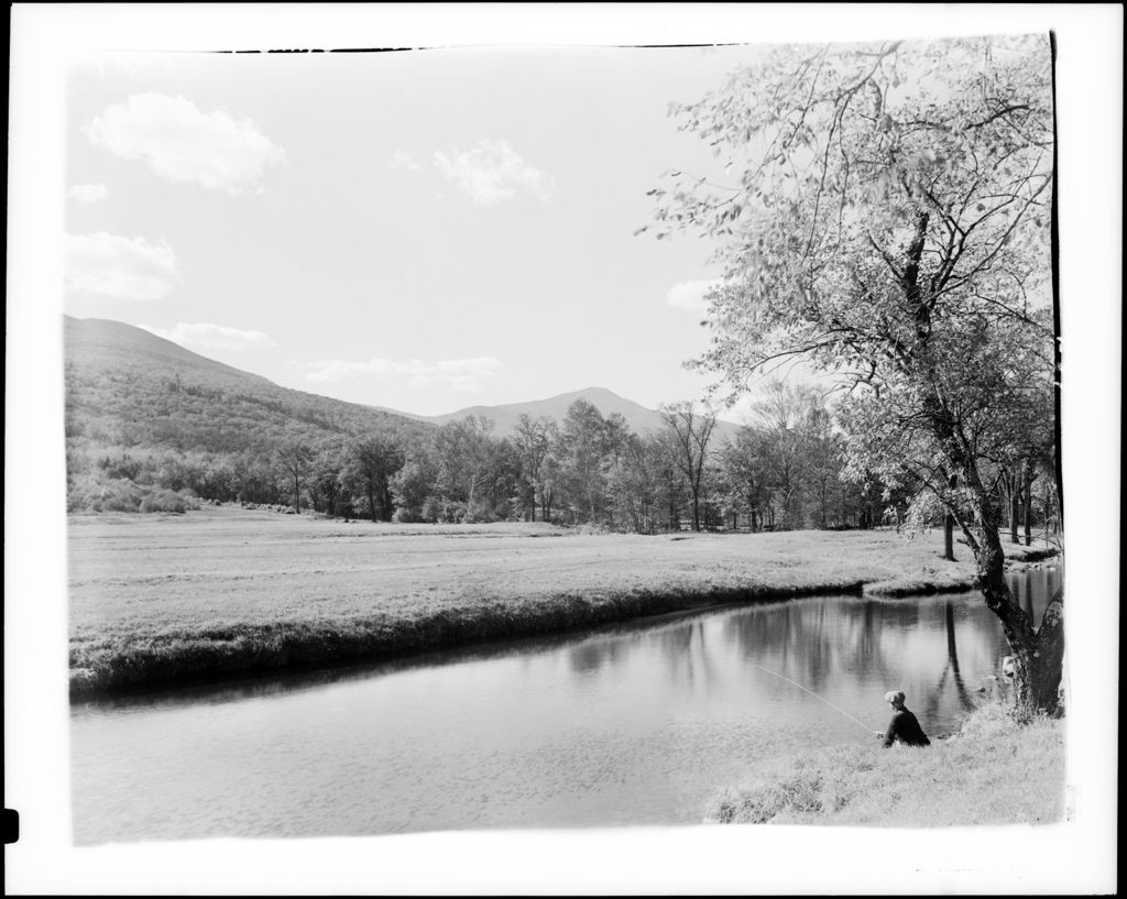 Miniature of Man Sitting On Stream Bank Fishing, Fields And Mountains In Distance