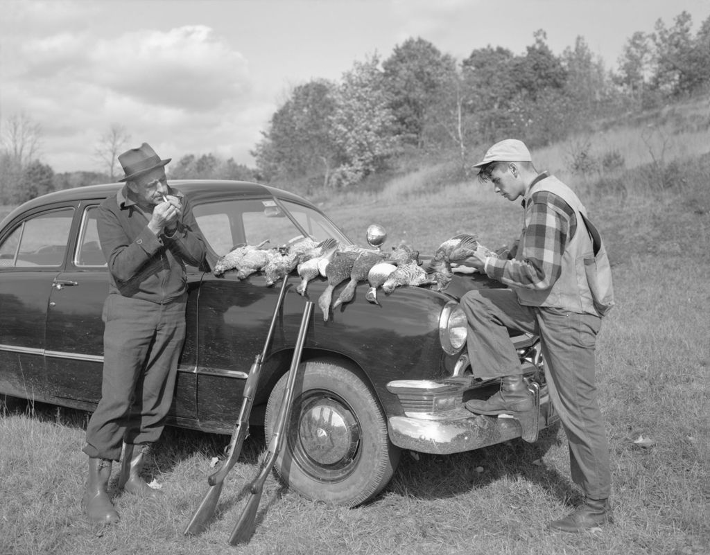 Miniature of Vern And Jim By Car, Vern Lights Pipe, Jim Looks Over Many Birds On Hood Of Car, Guns Lean Against Fender, Field Behind In Porter