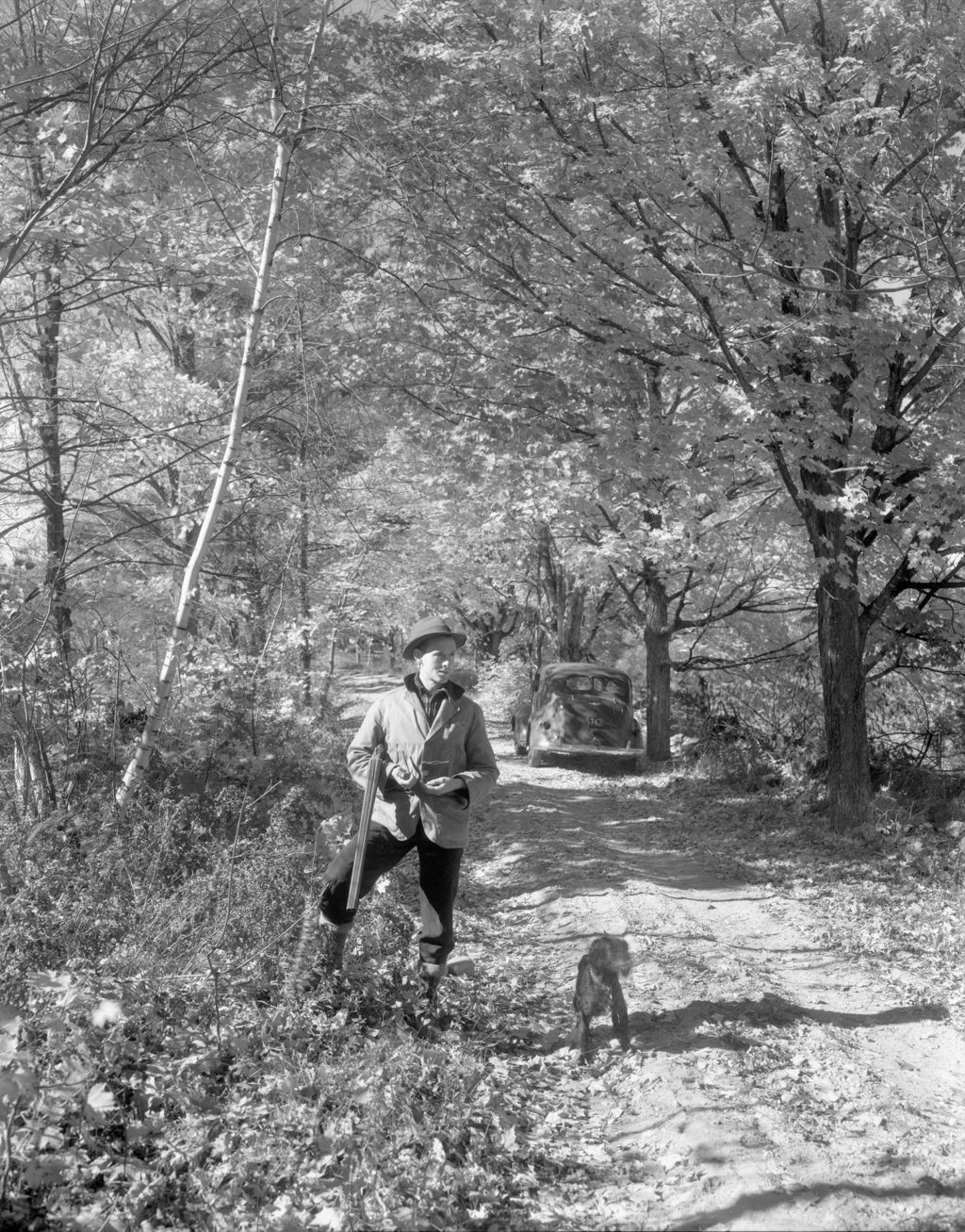 Miniature of Lester Stands On Side Of Woods Road Filling Pipe, Gun In Arm, Dog At Feet, Car Behind In Road