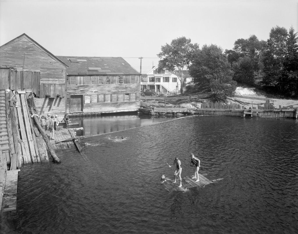 Miniature of Many Children Swimming, Sit Near Mill Or Float On Homemade Raft At Mill Pond, Partial View Of Village Behind In East Boothbay