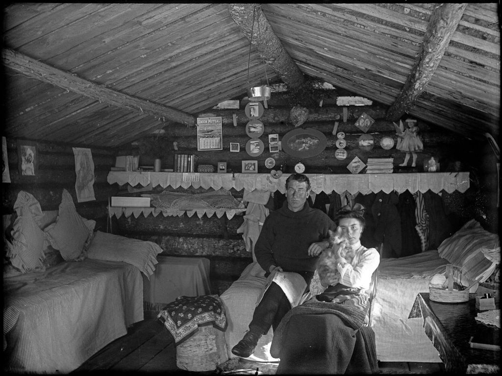 Miniature of Man and woman holding a cat seated in a small, decorated log cabin