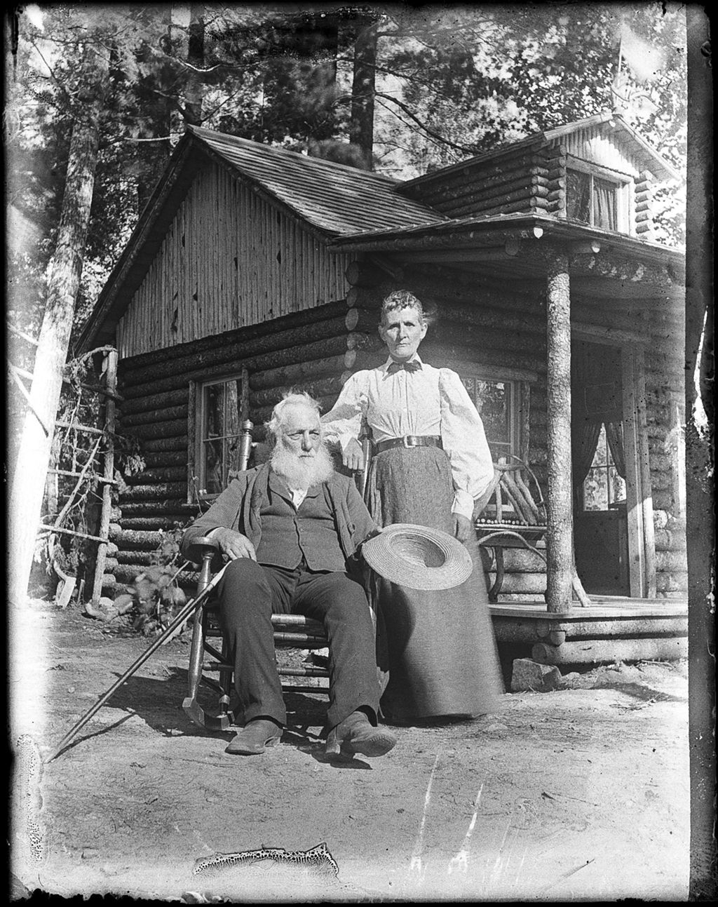 Miniature of Elderly, bearded man seated, with his wife standing beside him, outside of his log cabin home
